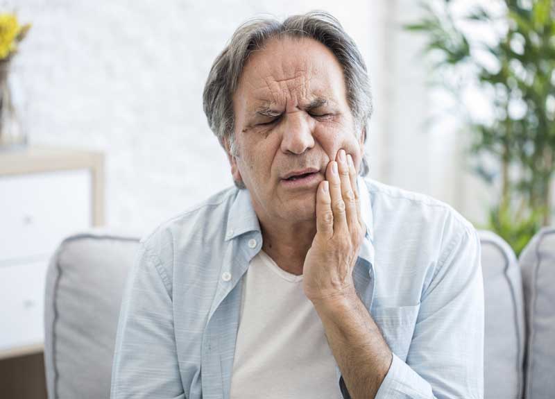 elderly man holding his hand to his mouth where there is pain