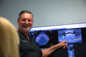Dr. Brand smiling at a patient as he points to her dental x-rays and talks to her about her All-On-4 dental implant procedure.