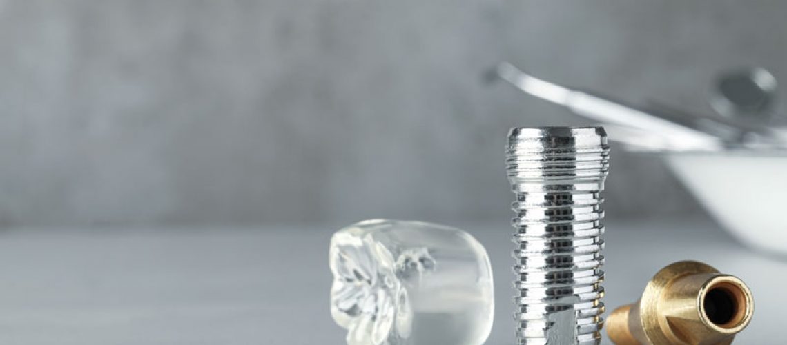 Dental implant pieces laying on a on a table, close up image of dental implant model. Reflecting off of the gloss table it shows all parts of a dental implants