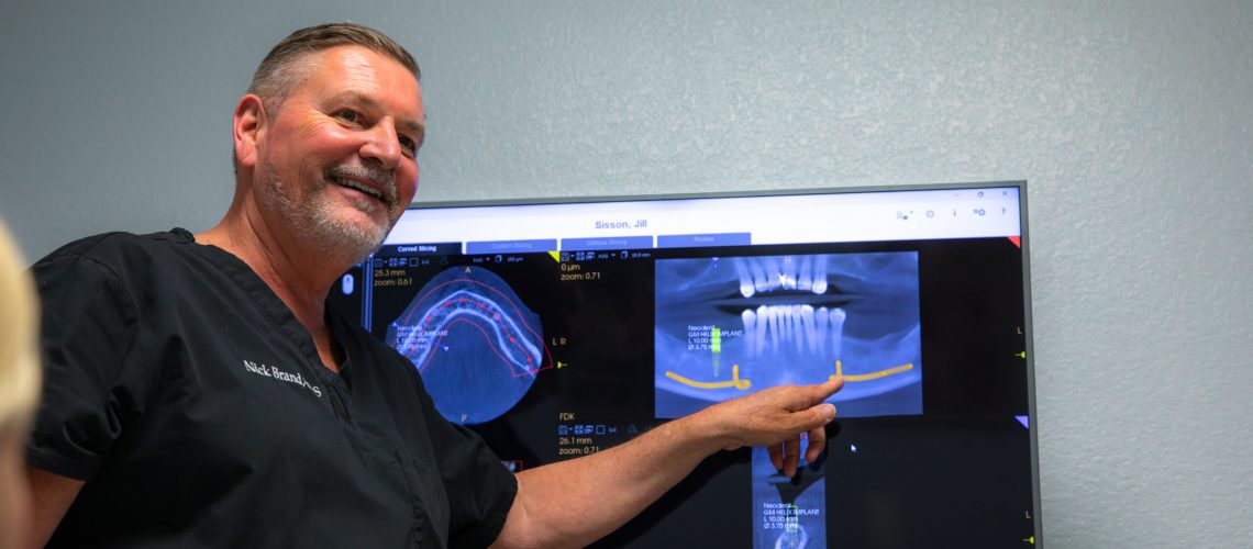 Dr. Brand smiling and pointing at a patients x-ray before their bone grafting procedure begins.