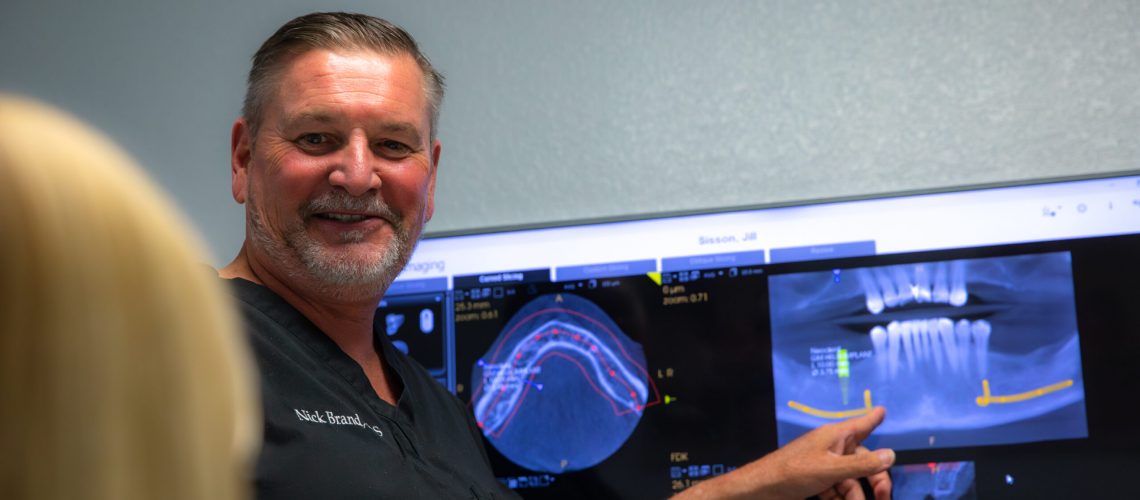 Dr. Brand smiling at a patient as he points to her dental x-rays and talks to her about her All-On-4 dental implant procedure.