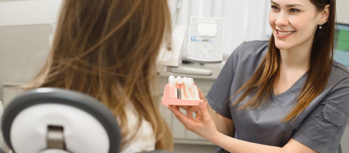 a dental professional showing a patient a dental implant model so she can explain to her how she can have a comprehensive dental implant procedure.