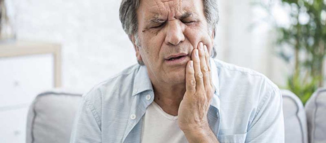 elderly man holding his hand to his mouth where there is pain